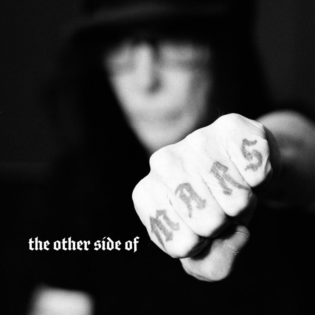 other side of mars album cover - mick mars punching with left hand to show knuckle tattoos